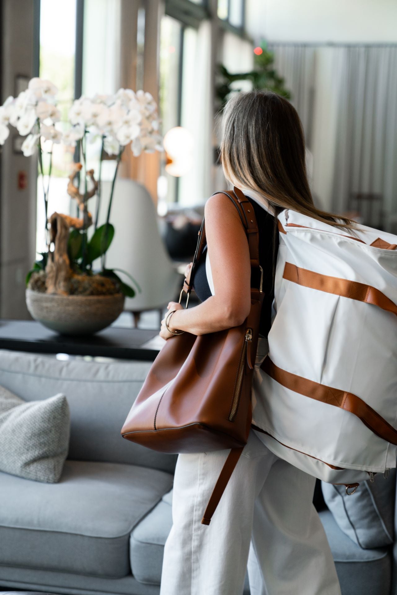 Stylish woman carrying a convertible duffle bag and a brown tote in a modern lounge, showcasing versatile travel gear.